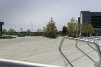 a large plaza with metal benches and tables and trees, on the outside of a tall building