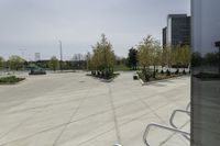 a large plaza with metal benches and tables and trees, on the outside of a tall building