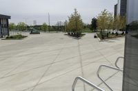 a large plaza with metal benches and tables and trees, on the outside of a tall building