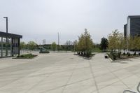 a large plaza with metal benches and tables and trees, on the outside of a tall building