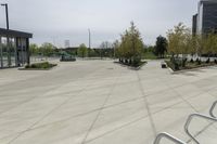 a large plaza with metal benches and tables and trees, on the outside of a tall building