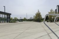 a large plaza with metal benches and tables and trees, on the outside of a tall building