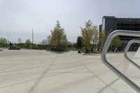 a large plaza with metal benches and tables and trees, on the outside of a tall building