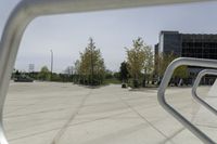 a large plaza with metal benches and tables and trees, on the outside of a tall building