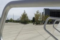 a large plaza with metal benches and tables and trees, on the outside of a tall building