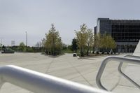 a large plaza with metal benches and tables and trees, on the outside of a tall building