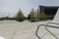 a large plaza with metal benches and tables and trees, on the outside of a tall building