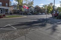 a canadian flag is flying in the air over a city street with parked cars and buildings