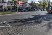 a canadian flag is flying in the air over a city street with parked cars and buildings