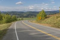 there is a yellow and black road sign on a hill side with mountains in the background