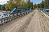 a metal bridge crosses over a dirt road near trees and a river in a remote region