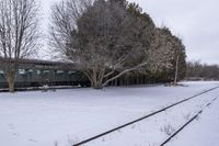 a snow covered field with a train on the tracks and trees in the background next to the track