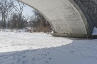 snow covers a road bridge in the wintertime with footprints in the snow, a bench and trees