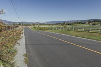 an empty road with fences and bushes in the foreground and mountains in the distance