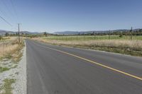 an empty road with fences and bushes in the foreground and mountains in the distance