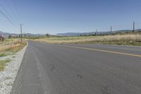 an empty road with fences and bushes in the foreground and mountains in the distance