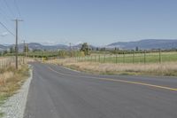 an empty road with fences and bushes in the foreground and mountains in the distance