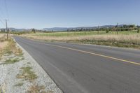 an empty road with fences and bushes in the foreground and mountains in the distance