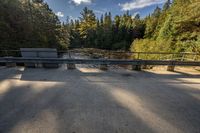 a bridge over the water in front of trees with a bench in the foreground