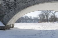 this stone bridge is over a snowy river near some trees and shrubs with footprints on the snow