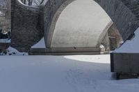 a snow covered stone arch under a bridge with snow around it and the ground with tracks on it