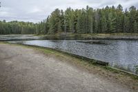 there are some trees on the side of the lake that surround this road and a wooden bench