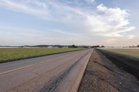 a view of a large empty road with grass on the side of the road in the background