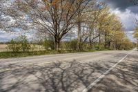 the empty street is lined with trees in the country side view and sky background with clouds