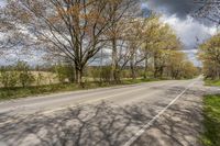 the empty street is lined with trees in the country side view and sky background with clouds