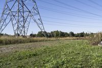 an old tractor sits under an over - grown, electric power line with a large utility tower