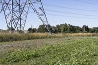 an old tractor sits under an over - grown, electric power line with a large utility tower