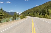 a scenic and beautiful highway lined with pine trees and mountains in the background and a body of water behind