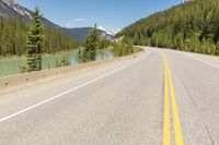 a scenic and beautiful highway lined with pine trees and mountains in the background and a body of water behind