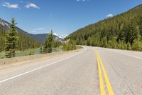 a scenic and beautiful highway lined with pine trees and mountains in the background and a body of water behind