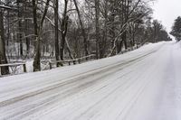 a snowy road is lined with snow and some trees in the background are without leaves