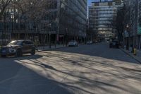 an empty city street in front of tall buildings with parked cars on it's side