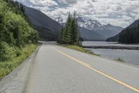 a road by the river leading up to mountains and some pine trees on both sides