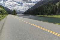 a road by the river leading up to mountains and some pine trees on both sides