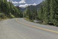 a person on a motorcycle rides on a mountain road through the woods, and there are mountains and trees in the background