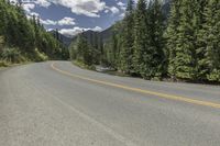 a person on a motorcycle rides on a mountain road through the woods, and there are mountains and trees in the background