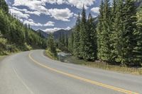 a person on a motorcycle rides on a mountain road through the woods, and there are mountains and trees in the background