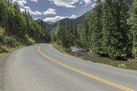 a person on a motorcycle rides on a mountain road through the woods, and there are mountains and trees in the background