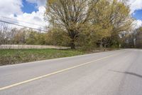 a rural road is lined with trees and bushes, and the roadway ends in empty