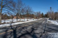 an empty street lined with trees and snow covered road side near a red brick home