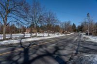 an empty street lined with trees and snow covered road side near a red brick home