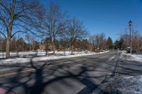 an empty street lined with trees and snow covered road side near a red brick home