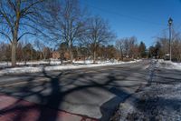 an empty street lined with trees and snow covered road side near a red brick home