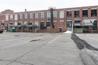 the empty parking lot has only snow on the ground in front of an old brick factory