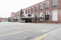 the empty parking lot has only snow on the ground in front of an old brick factory