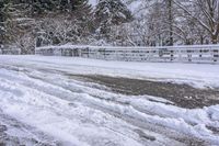 a bunch of snow is piled onto the road in front of a wooden bridge near a forest